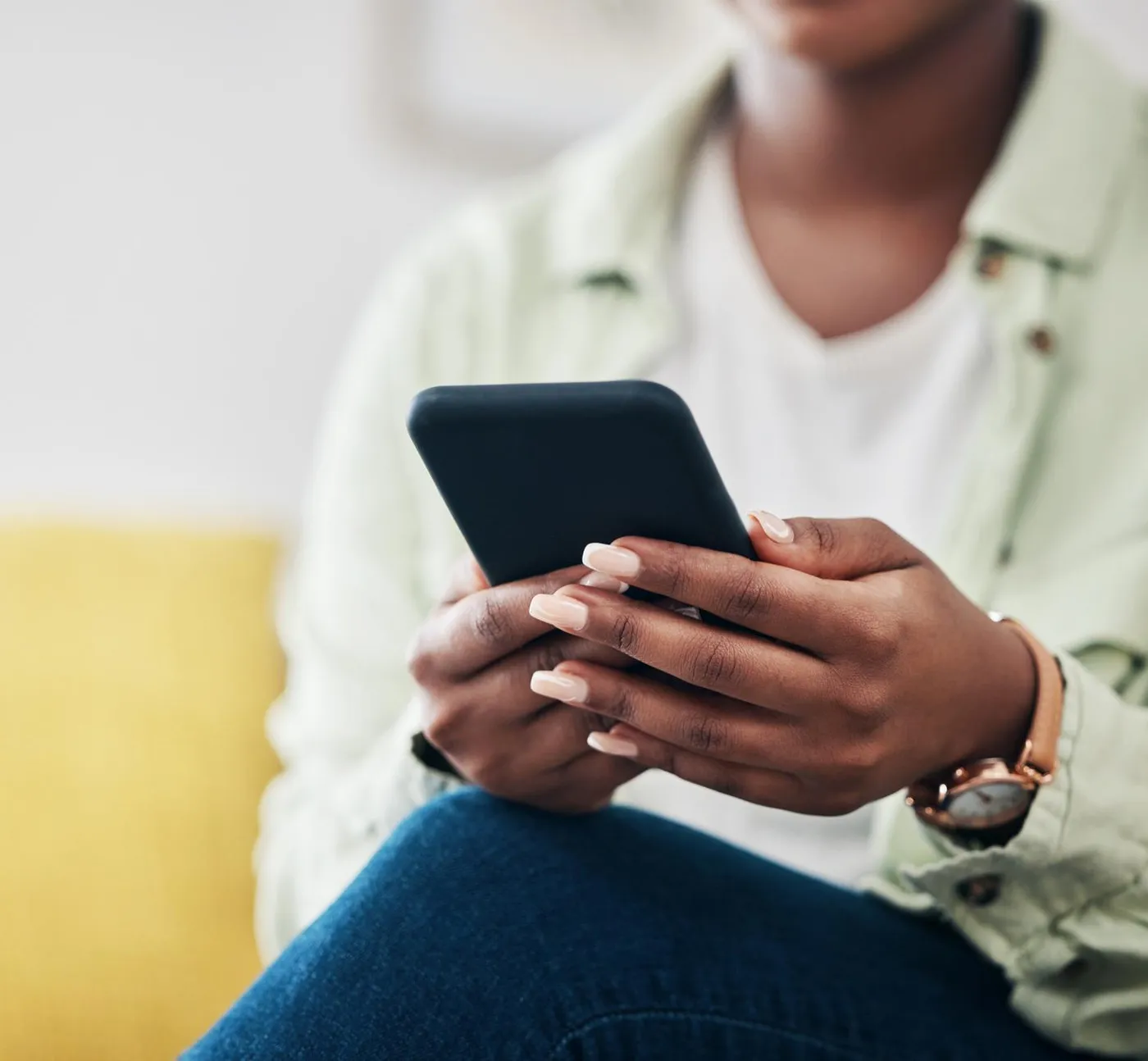 A woman sits with her phone in both hands, typing.