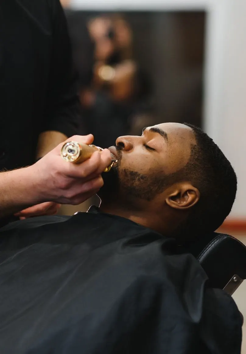 A barber lines up a client's beard with clippers.